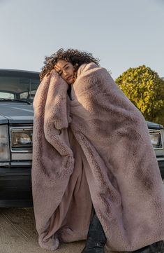 a woman wrapped up in a blanket sitting next to a parked car with her hands on her head