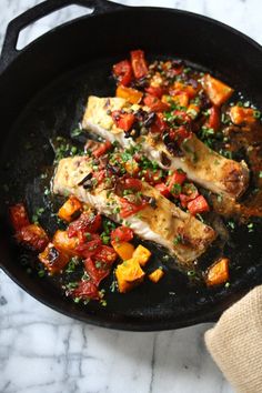 a skillet filled with chicken and vegetables on top of a marble countertop next to a wooden utensil