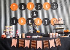 an orange and black halloween dessert table with trick or treat decorations on the wall behind it