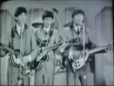 three men are playing guitars and singing into microphones in front of a television screen