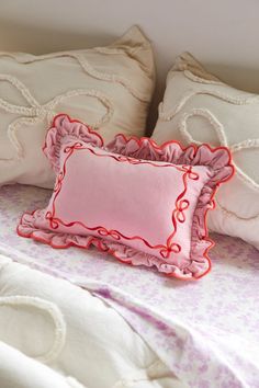 two pillows on a bed with pink and white sheets, one has a red scalloped edge