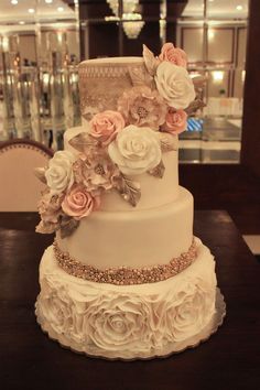 a three tiered wedding cake with pink flowers on the top and gold sequins