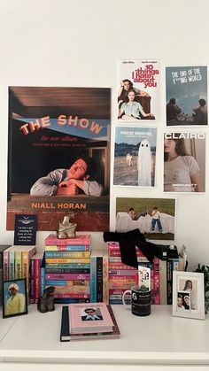 a white desk topped with lots of books and magazines next to pictures on the wall