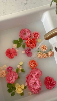 pink and yellow flowers are being washed in a sink