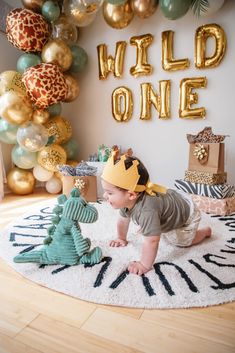 a baby is crawling on the floor in front of a wall with gold and green balloons