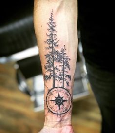 a man with a compass and trees tattoo on his arm