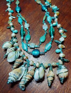 A unique, one of a kind, handmade three strand necklace that will really attract some attention. Aqua colored copper wire is wrapped by hand around multiple types of ocean shells, combined with genuine freshwater pearls, stones and glass beads. Beautiful shades of sea and sand make a true statement piece. Ocean Shells, Three Strand Necklace, Stone Statement Necklace, Aqua Color, Beach Theme, Multi Strand Necklace, Strand Necklace, Multi Strand, Beach Themes