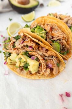 two shredded pork tacos with avocado and cilantro on the side