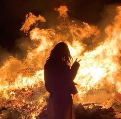 a woman standing in front of a fire with lots of flames around her and pointing at something