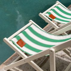 two green and white striped lawn chairs next to a pool with water in the background