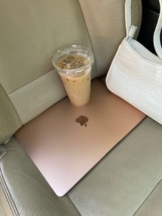 an apple laptop computer sitting on top of a car seat next to a cup of coffee