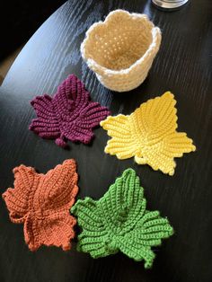 four crocheted leaves sitting on top of a wooden table next to a bowl