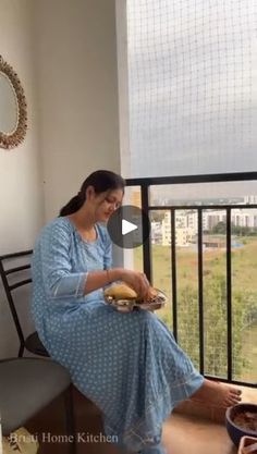 a woman sitting on top of a chair next to a window holding a plate of food