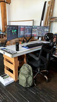 two computer monitors sitting on top of a wooden desk next to a bag and backpack