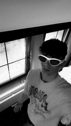 a young man wearing sunglasses sitting in front of a window