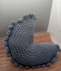 a crocheted gray pillow sitting on top of a wooden floor next to a white wall