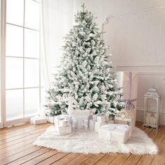 a white christmas tree with presents under it on a wooden floor next to a window