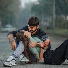 a man and woman sitting on the ground with their arms around each other as they kiss