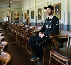 a man sitting on top of a wooden chair in a room filled with lots of chairs