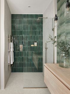 a bathroom with green tiles on the shower wall and wooden countertop, along with a glass vase filled with flowers