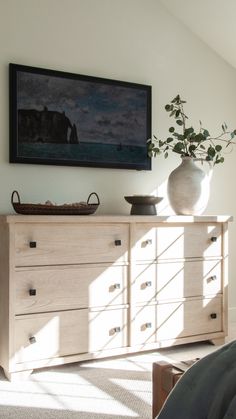 a white vase sitting on top of a wooden dresser next to a painting above it