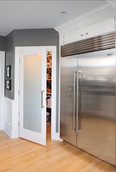 an empty kitchen with stainless steel refrigerator and white cabinets, along with hardwood flooring