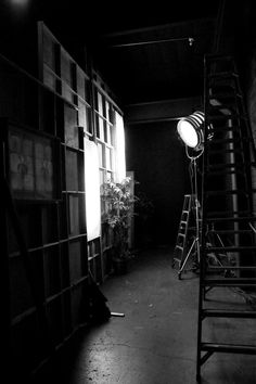 a black and white photo of a ladder in a dark room with light coming through the window