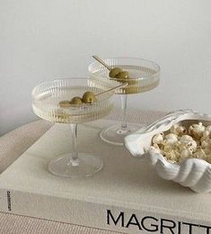 two martini glasses with olives in them on top of a book