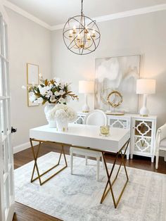 a white dining room table with gold accents and flowers in vases on the top