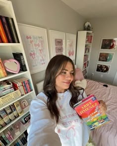 a woman sitting on a bed holding a book in her hand and smiling at the camera