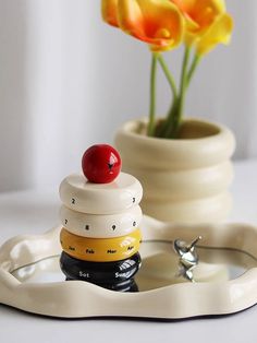 a white vase with yellow flowers in it and a small stack of rings on the tray