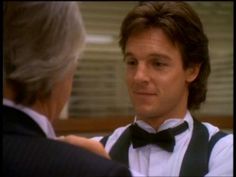 a man wearing a bow tie talking to an older person in a suit and vest