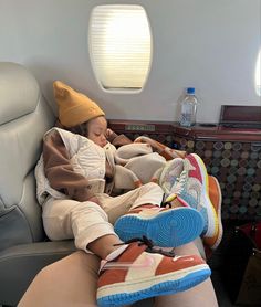 a child sleeping on an airplane seat with his feet propped up against the back of another person's leg