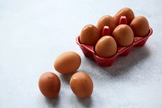 six eggs in a red carton on a white surface