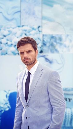 a man wearing a suit and tie standing in front of a wall with paintings on it