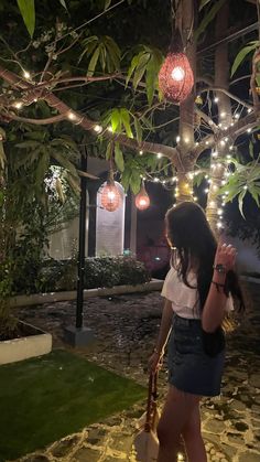 a woman standing under a tree with some lights hanging from it's branches in the background