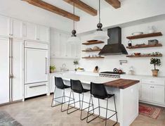 a large kitchen with white cabinets and wooden beams on the ceiling, along with black bar stools