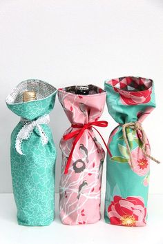 three different types of wine bottles wrapped in colorful fabric and tied with red ribbon, sitting on a white surface