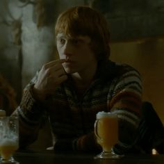 a young man sitting at a table with two beer mugs in front of him