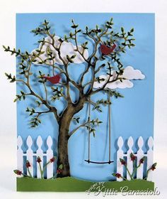 a card with a tree and two birds sitting on the branches, in front of a white picket fence