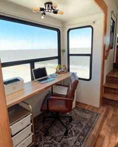 a desk with a laptop on top of it next to an open window overlooking the ocean