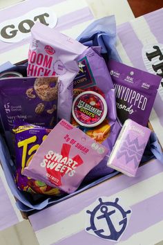 an open box filled with snacks on top of a purple and white striped tablecloth