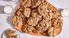 an orange plate with cookies and two glasses of milk next to it on a white table