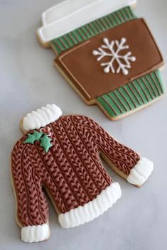 two decorated cookies are sitting on a table next to each other, one is wearing a sweater and the other has a snowflake