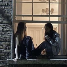 two people sitting on a window sill looking out at the street and building in front of them