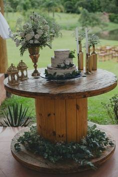 a wooden table topped with a cake covered in flowers and greenery next to a lush green field