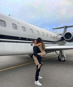 a man and woman kissing in front of an airplane on the tarmac at an airport