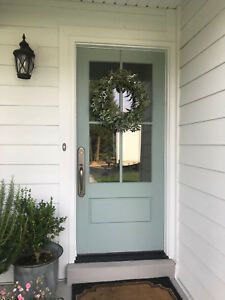 a blue front door with a wreath on it and two potted plants next to it