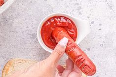 a person holding a hot dog in front of a bowl of ketchup and bread