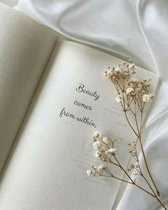 an open book with some flowers on top of it and the words beauty comes from within